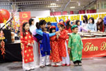 5 children wearing bright traditional vietnamese costumes, a woman passing a microphone to one of the children