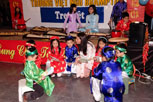 A young woman story telling to 6 small children sitting in a circle.  The children are wearing traditional vietnamese cosumes.